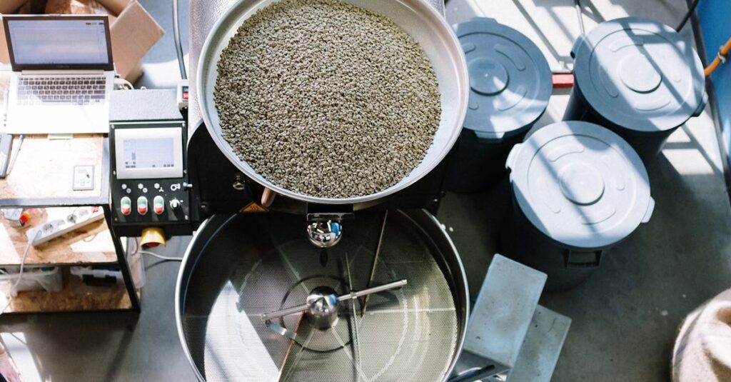 Overhead view of industrial coffee roaster with raw beans in a workshop setting.