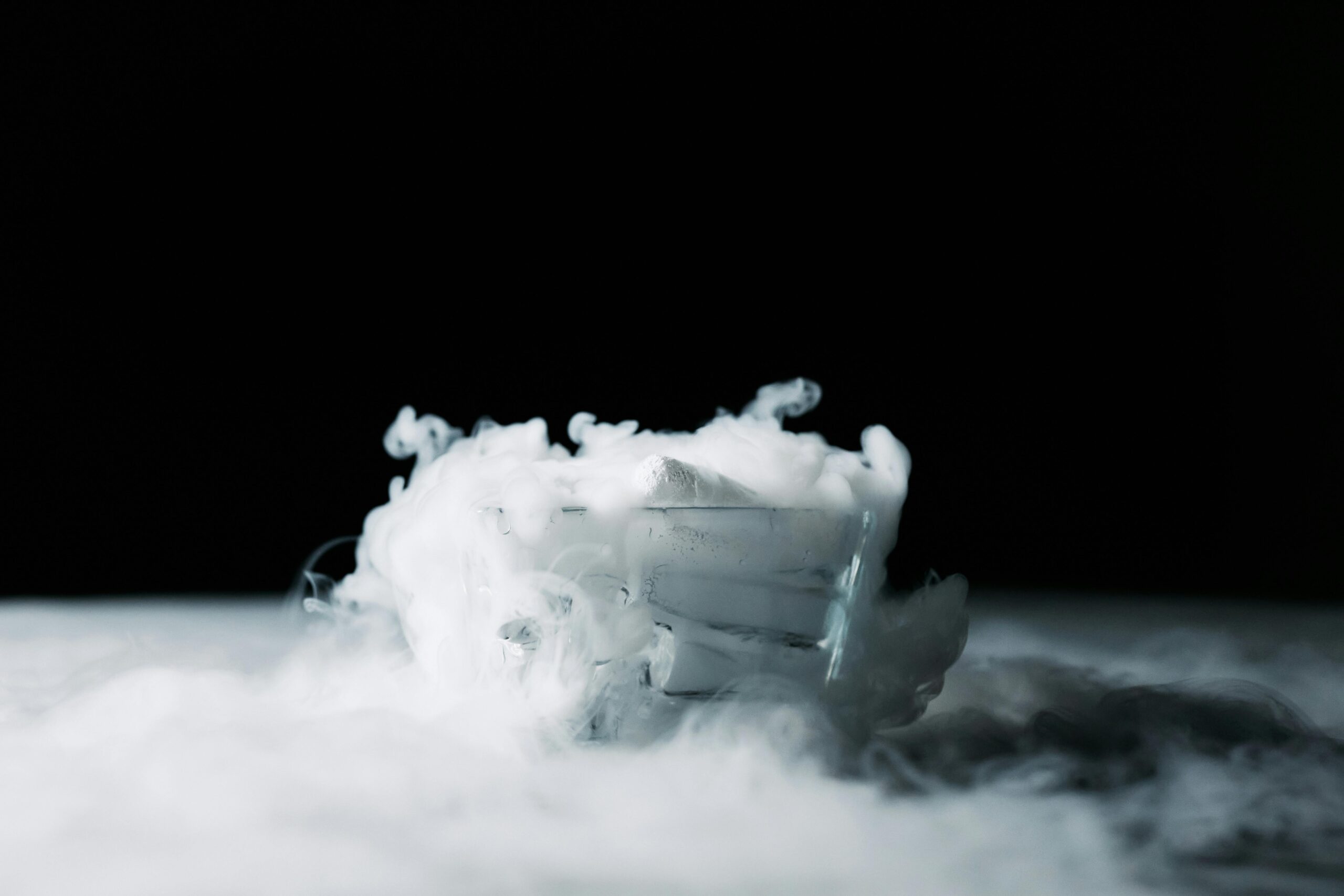 Mystical swirling vapor emanating from dry ice in a glass on a black background.